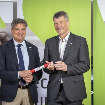 TU Wien-Rektor Jens Schneider (links) übergibt die Präsidentschaft der TU Austria an TU Graz-Rektor Horst Bischof. Bildquelle: Lunghammer - TU Austria Zwei Herren in Anzügen lächeln in die Kamera. Der linke übergibt dem rechten ein Staffelholz.