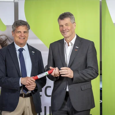 TU Wien-Rektor Jens Schneider (links) übergibt die Präsidentschaft der TU Austria an TU Graz-Rektor Horst Bischof. Bildquelle: Lunghammer - TU Austria Zwei Herren in Anzügen lächeln in die Kamera. Der linke übergibt dem rechten ein Staffelholz.